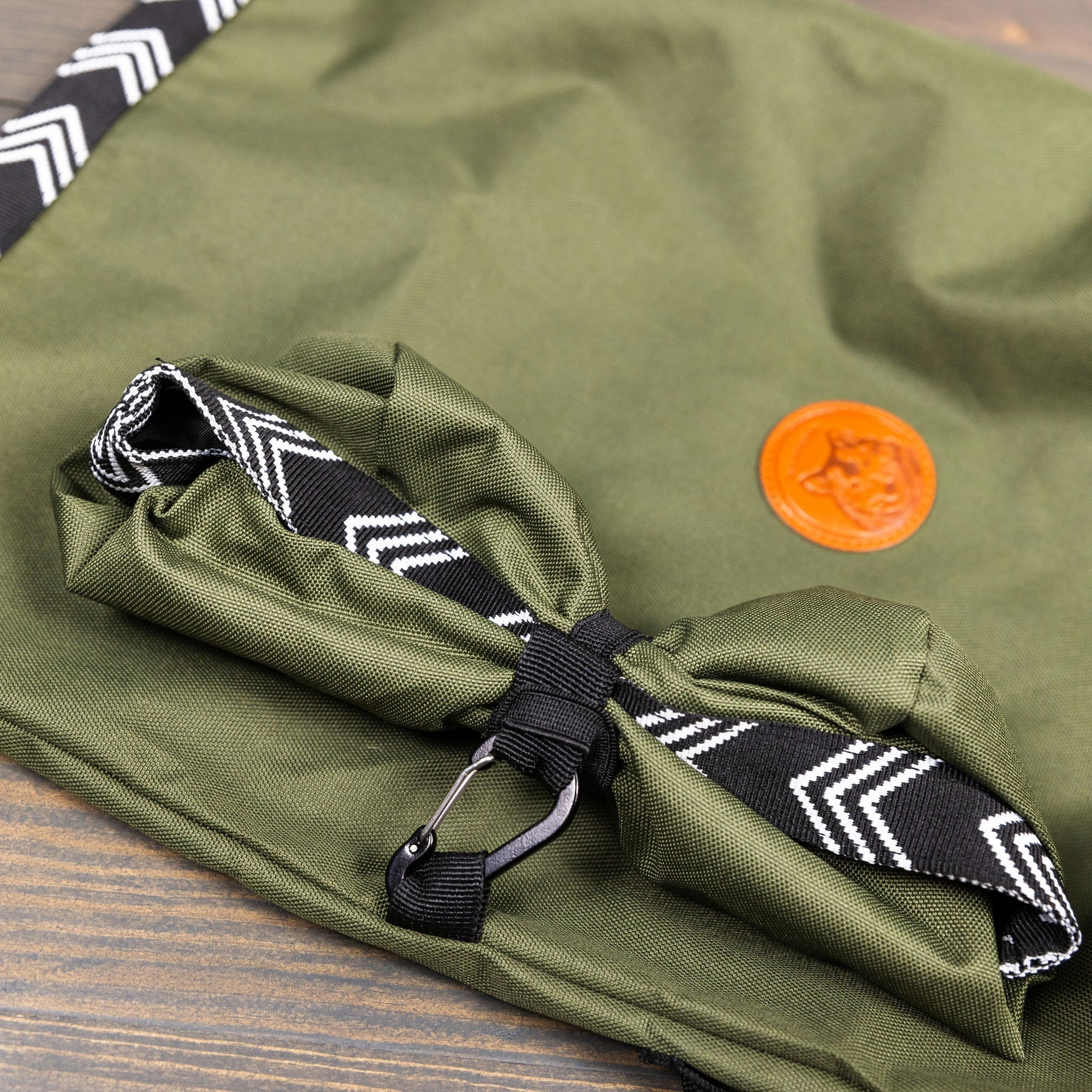 Close-up of olive green dog food bag rolled up, secured with a black chevron strap and carabiner clip