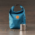 Load image into Gallery viewer, Pacific blue dog food storage bag with roll-top closure and orange branded patch, placed next to a stainless steel cup
